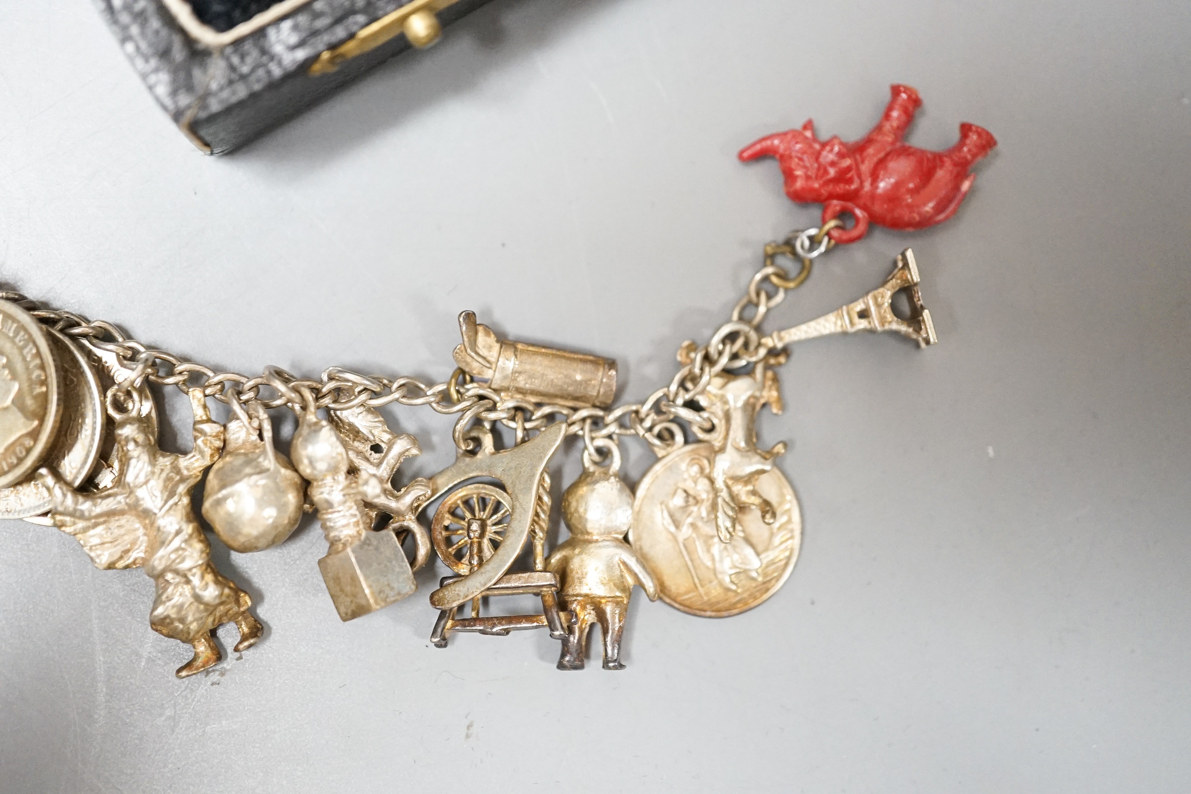 A 1930's cased silver christening set, comprising an egg cup, spoon and napkin ring, together with a white metal charm bracelet hung with assorted charms and coins including silver.